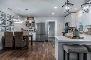 Une cuisine moderne dotée d’un îlot central, d’appareils électroménagers en acier inoxydable et de luminaires suspendus.