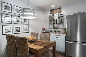 Una cocina con refrigerador de acero inoxidable, una mesa de comedor con sillas de mimbre y fotografías en blanco y negro enmarcadas en la pared.