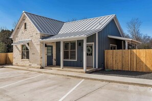 A two-story building with a stone facade, a metal roof, and a wooden fence. - Strawberry Suite - Fire Pit, BBQ Grill & more! (Fredericksburg)