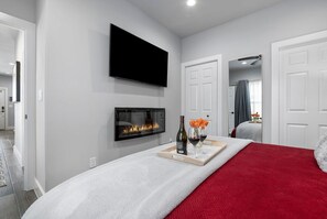 A bedroom with a TV, fireplace, and a tray with wine and flowers. - Strawberry Suite - Fire Pit, BBQ Grill & more! (Fredericksburg)