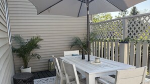 Un patio con una mesa y sillas blancas, un parasol grande y una valla con celosía.