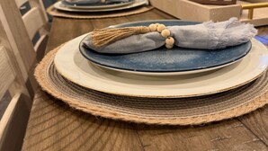 Una mesa de comedor con individuales, platos y un centro decorativo.