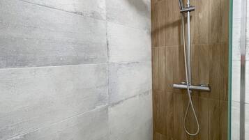 Una ducha con cabezal de ducha tipo lluvia y un cabezal de ducha de mano, suelo de madera y pared con azulejos.