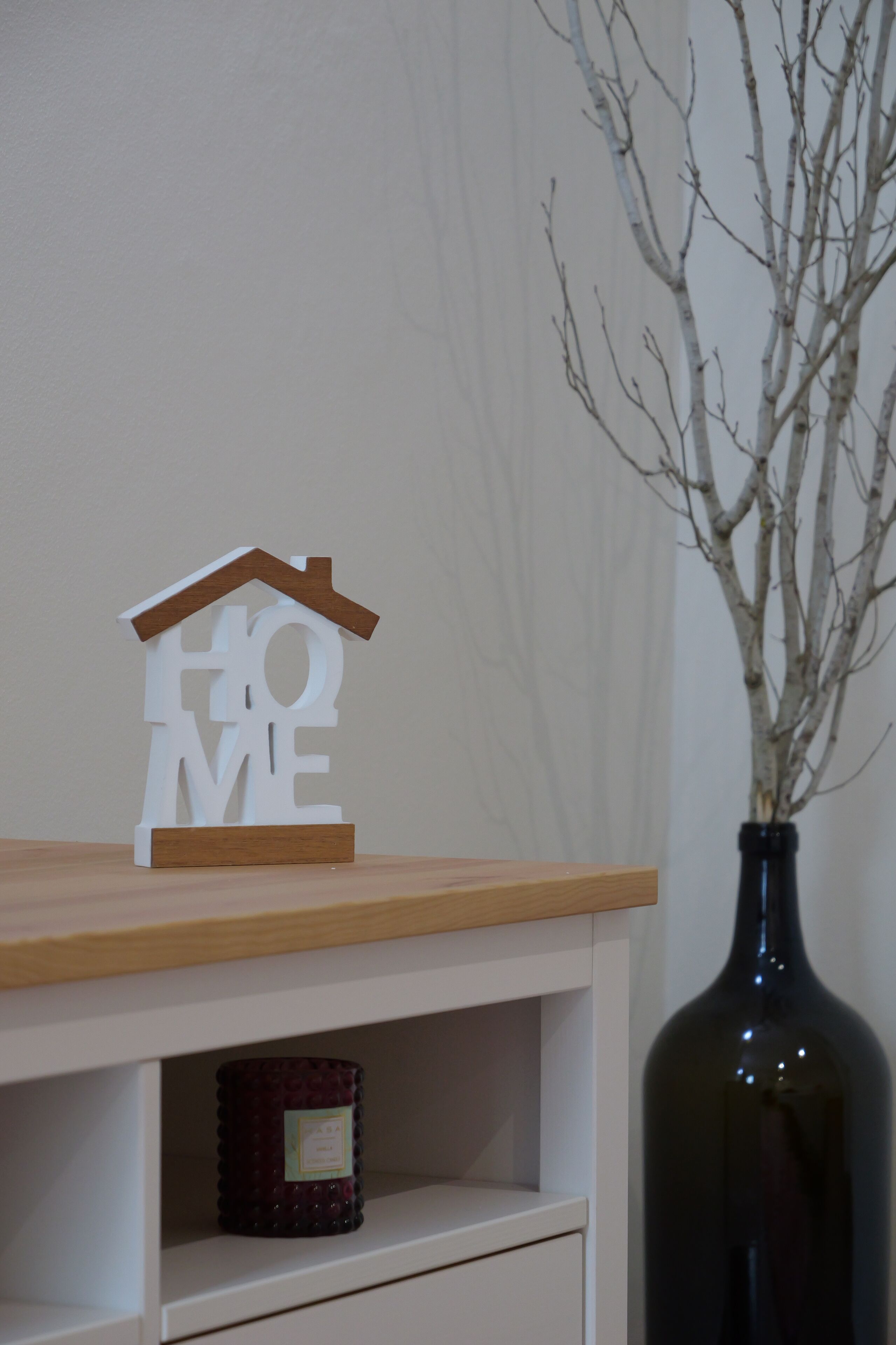 A wooden shelf with a house-shaped decoration, a dark bottle, and a small container.