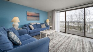 Een moderne woonkamer met een blauwe wand, twee banken, een salontafel en een grote glazen schuifdeur die leidt naar een balkon.