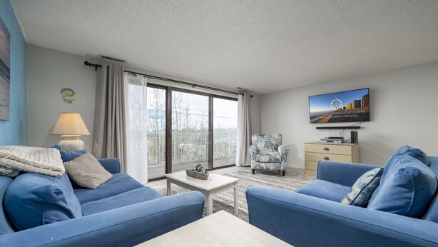 Een moderne woonkamer met blauwe banken, een witte salontafel en een televisie aan de muur.