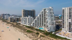 A beachfront hotel with modern architecture, a pool, and a beach view.