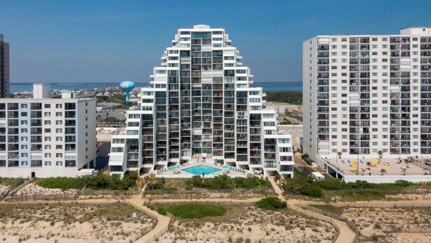 A beachfront hotel with a central swimming pool, multiple balconies, and a view of the beach.