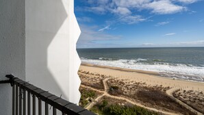 A balcony overlooking a beach with a clear sky and ocean waves.