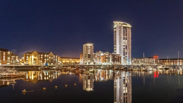 A waterfront cityscape with illuminated buildings and a marina. - Captivating 1-bed Apartment in Swansea (Swansea)