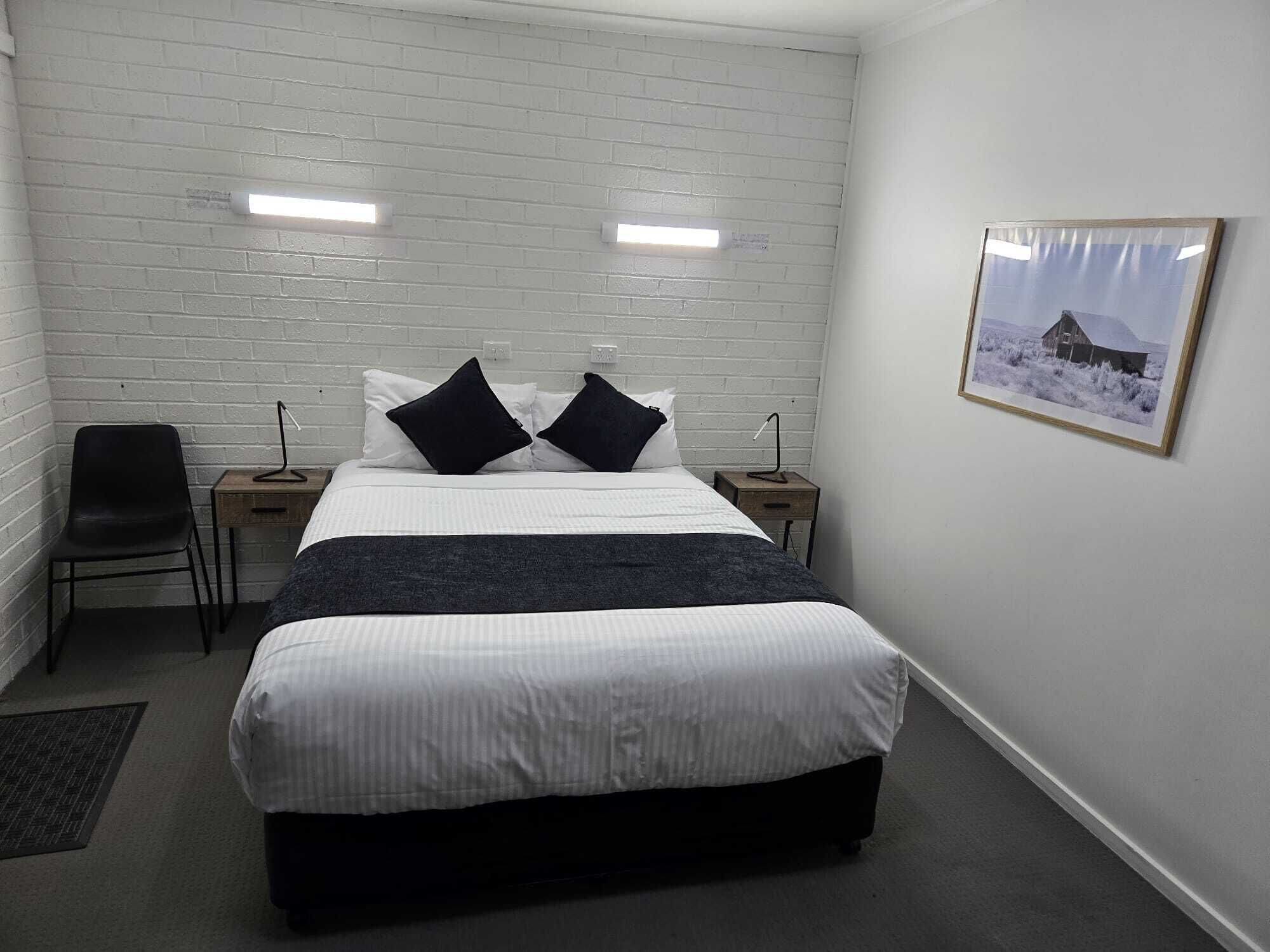 Ein Schlafzimmer mit einem großen Bett, zwei Nachttischen, einem Sessel und einem gerahmten Bild an der Wand.