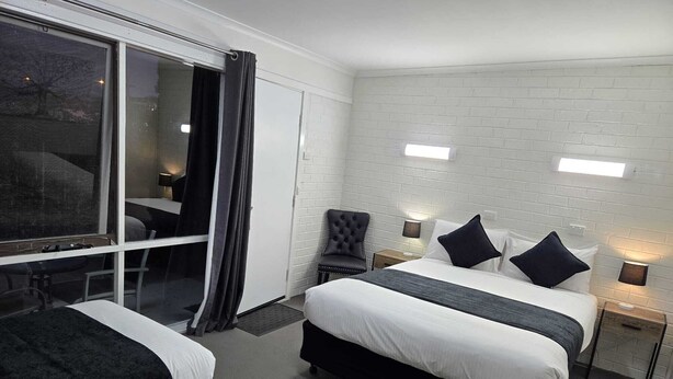 Habitación de hotel con dos camas, un ventanal con cortinas, una silla y una mesita.