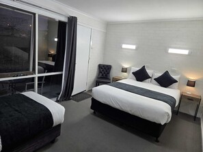 A hotel room with two beds, a large window with curtains, a chair, and a small table.