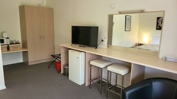 A compact hotel room with a kitchenette, a television, a mirror, and a small refrigerator.