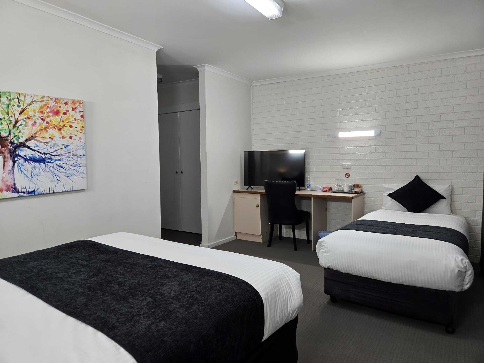 Habitación de hotel con dos camas, un escritorio con televisor, una silla y un cuadro en la pared.