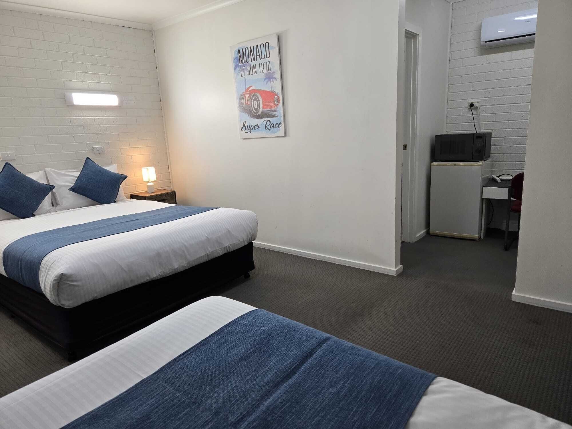 A hotel room with a bed, a desk, and a chair. There is a picture on the wall and an air conditioner above the desk.