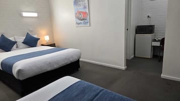 A hotel room with a bed, a desk, and a chair. There is a picture on the wall and an air conditioner above the desk.