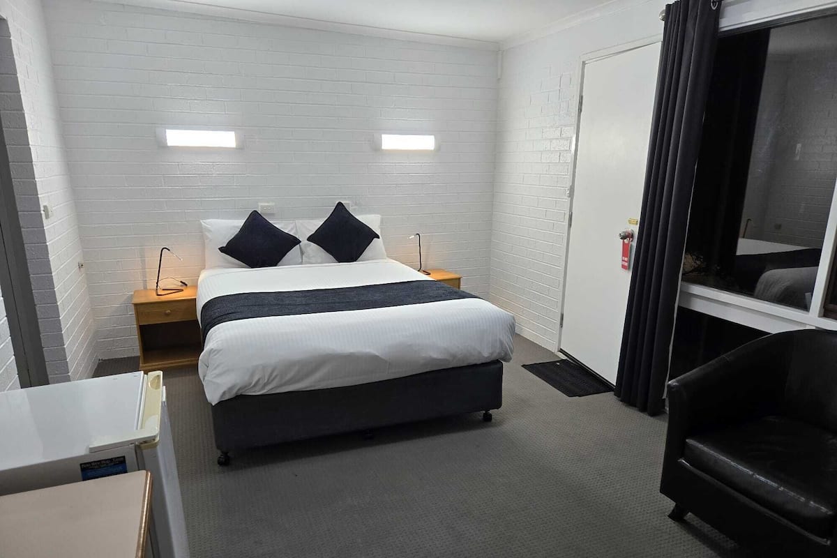 A hotel room with a bed, bedside tables, a desk, a chair, and a wardrobe.