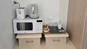 Una pequeña kitchenette con microondas, tostadora, hervidor de agua y cafetera sobre una encimera de madera.