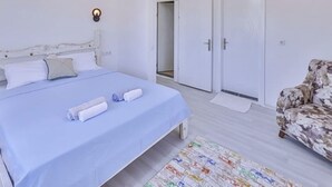 A bedroom with a bed, a ceiling fan, a door, and a patterned rug. - Kaya Apart  (Kas)