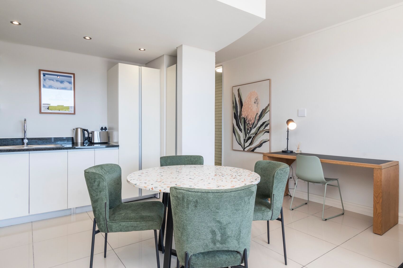 A modern kitchen with a round table and four chairs, a wooden desk, and a chair.