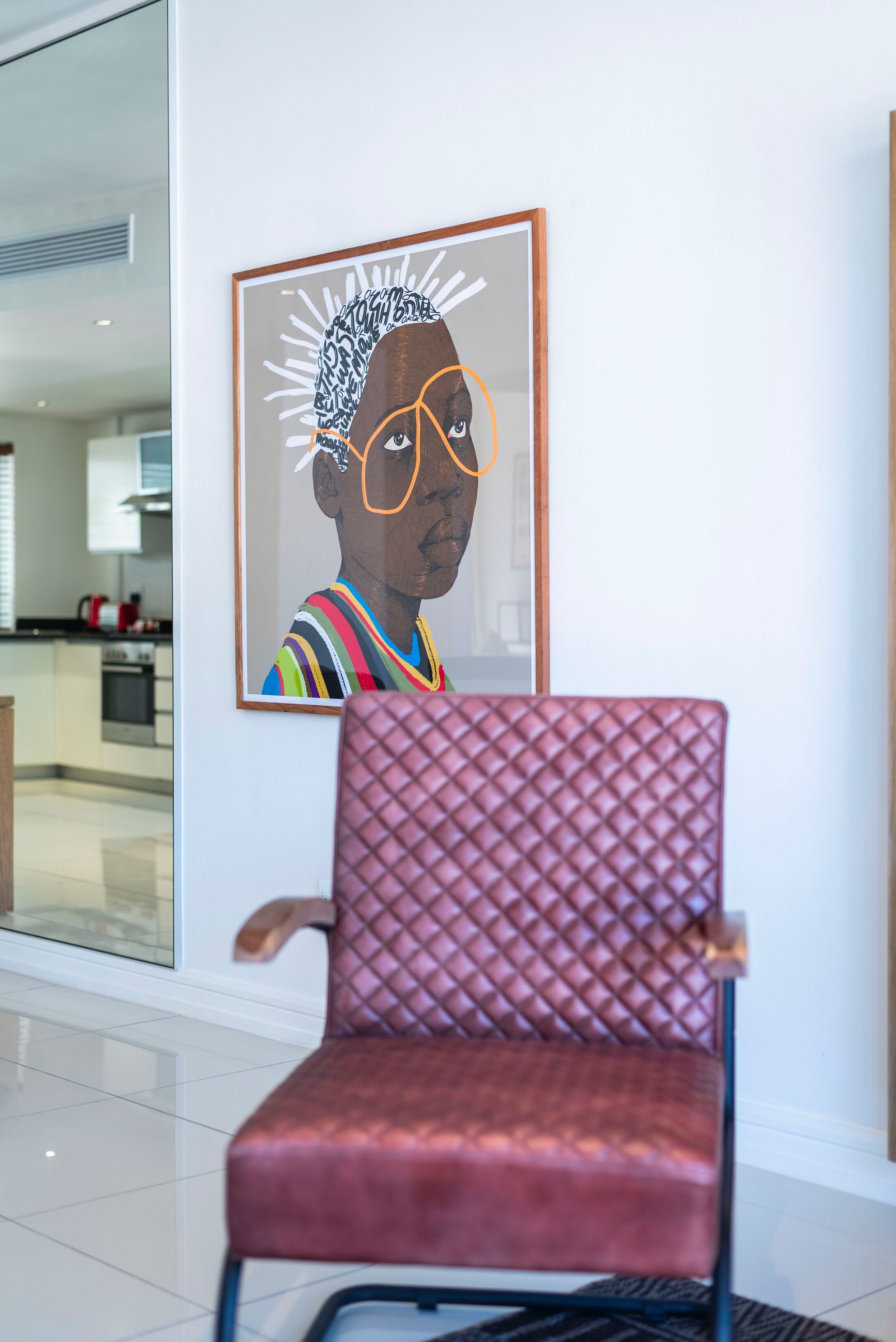 A modern interior with a red cushioned chair and a framed artwork on the wall.