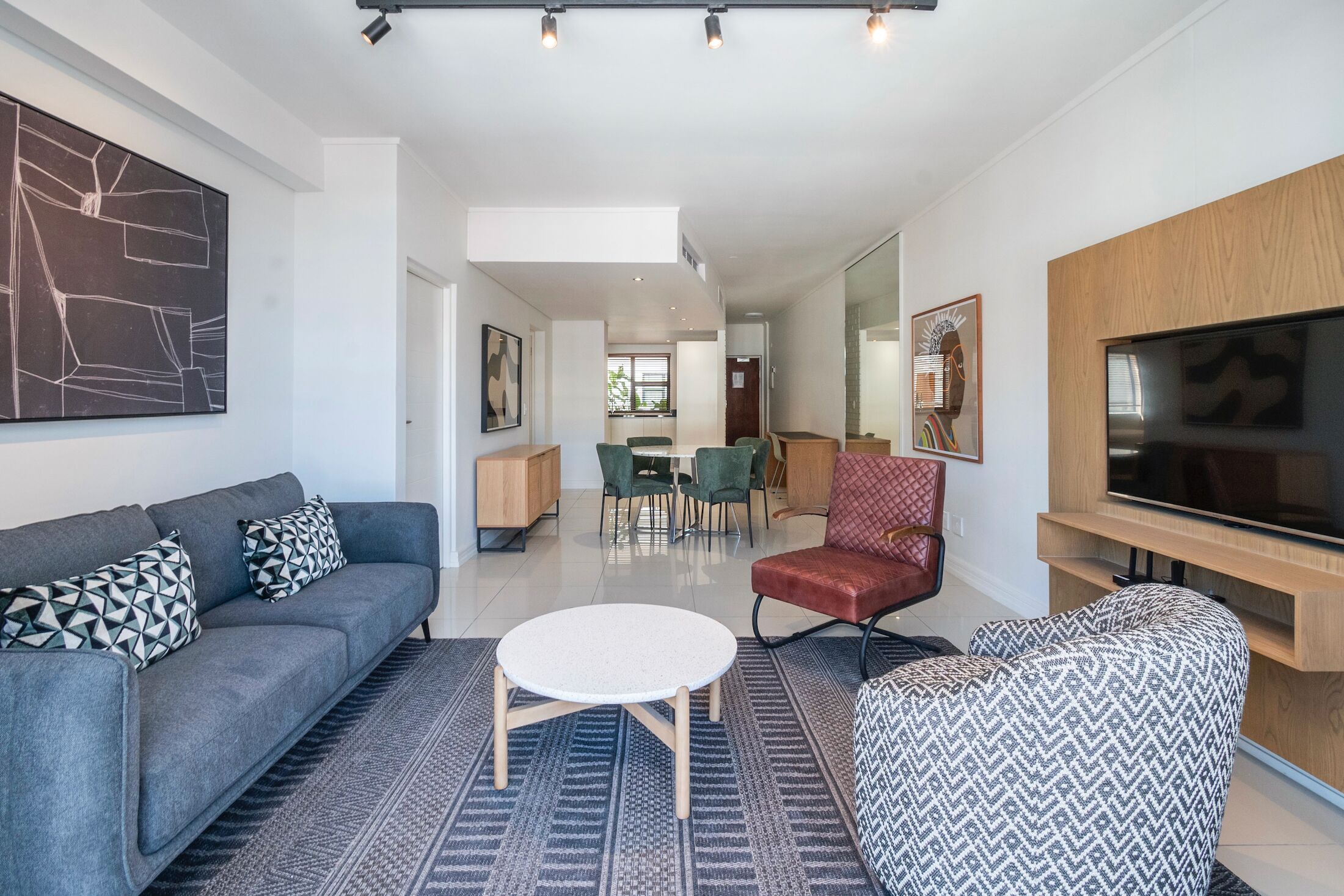 A modern living room with a sofa, armchair, round coffee table, and a flat-screen TV.