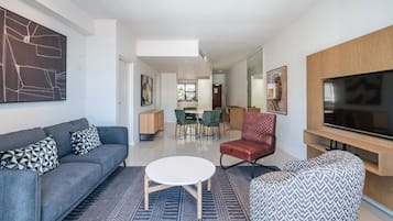 A modern living room with a sofa, armchair, round coffee table, and a flat-screen TV.