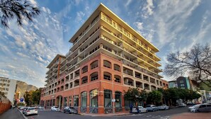 Een meerhoog hotel met een opvallende rode baksteenvoorgevel, meerdere balkons en een parkeerplaats ervoor.