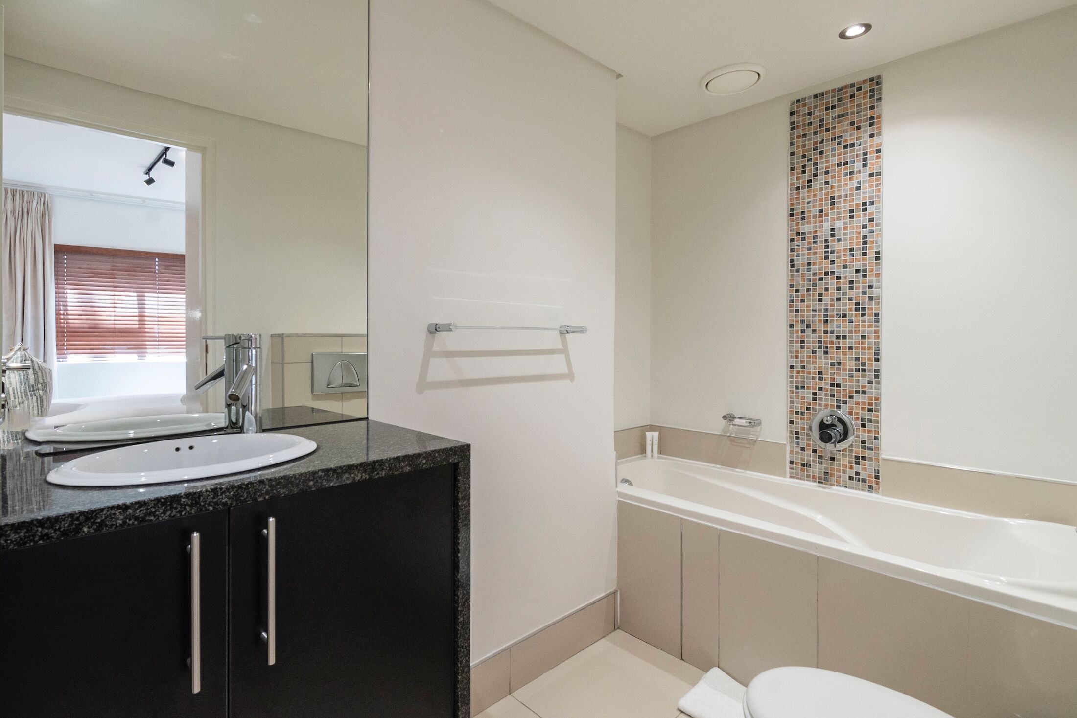A modern bathroom with a double sink vanity, a bathtub, and a toilet.