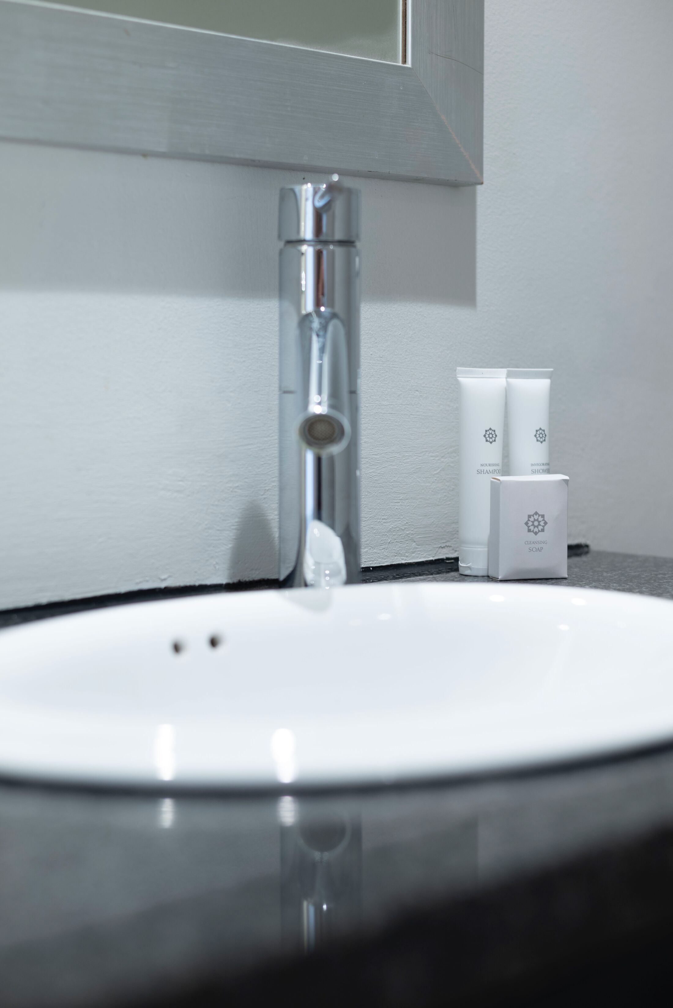 Un lavabo con un grifo cromado y dos botellas blancas de champú y jabón en la encimera.
