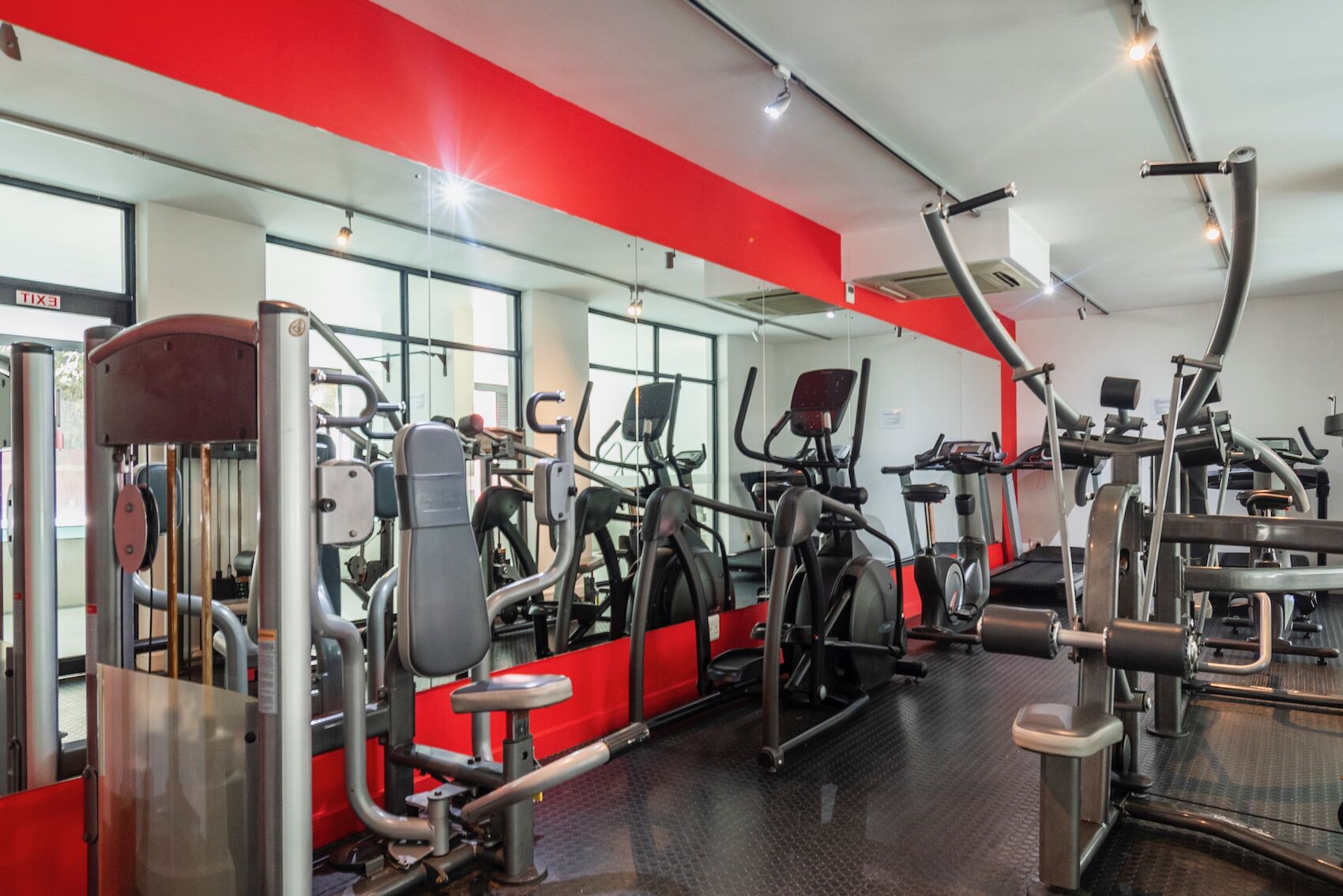 Un gimnasio con diversas máquinas de ejercicio, espejos y una pared de acento en rojo.