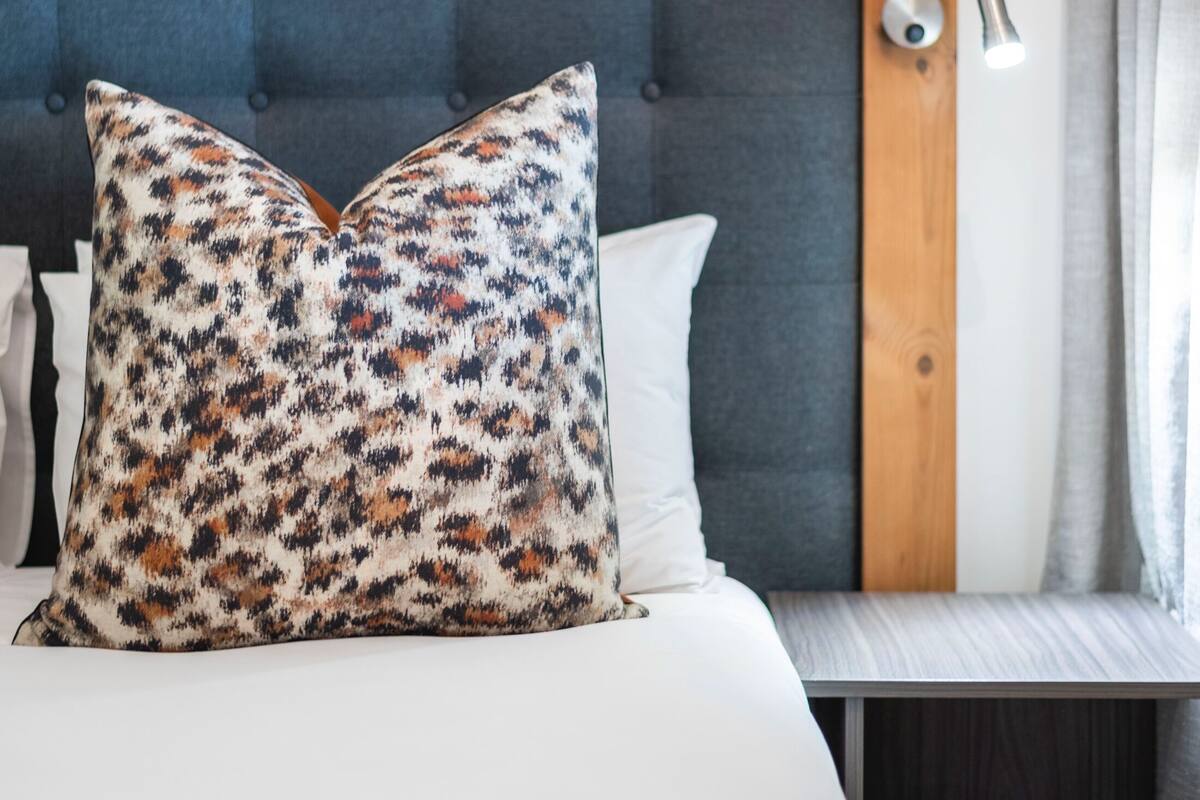 Een keurig opgemaakt bed met een gestreept kussen, een houten hoofdbord en een nachtkastje.