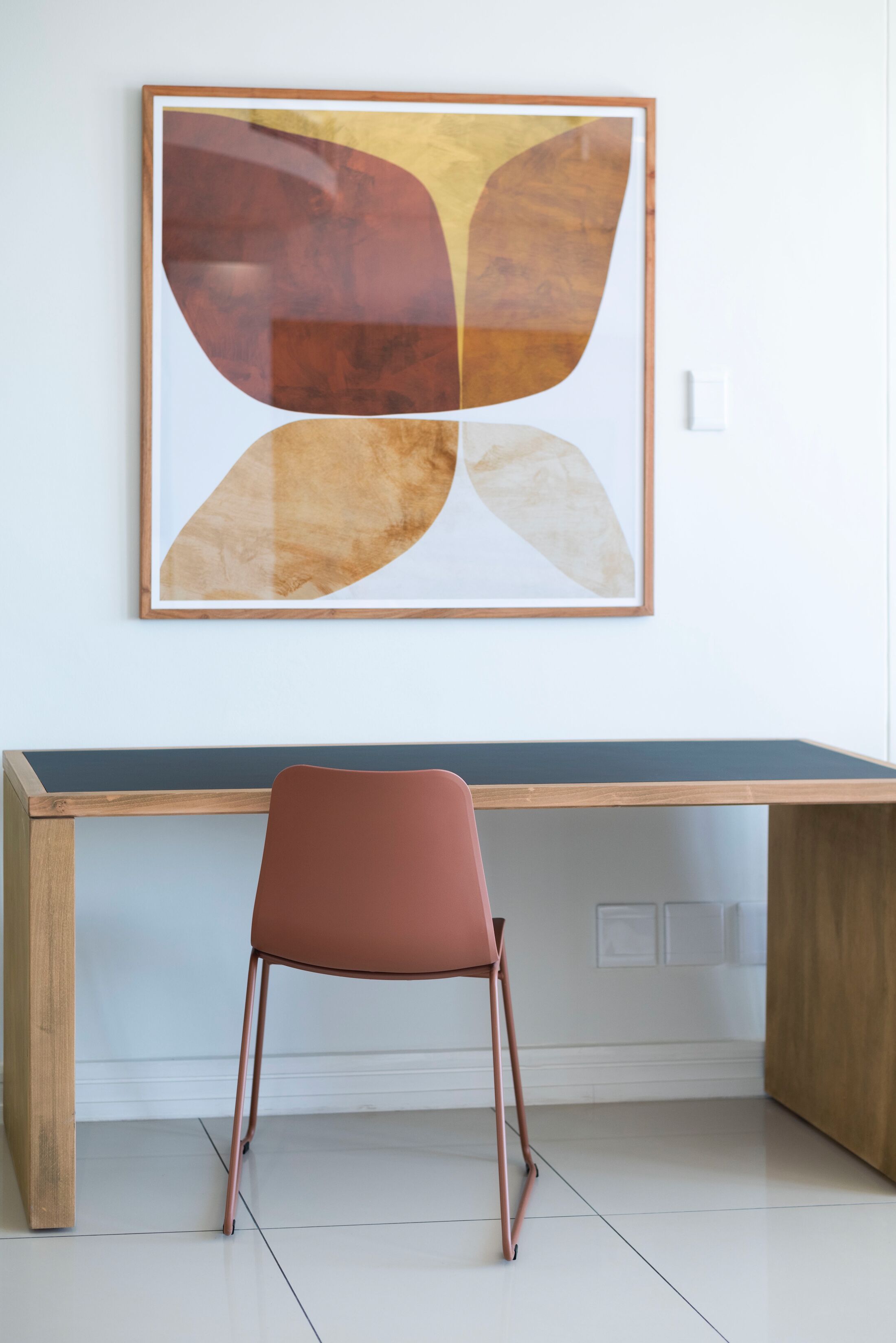 A modern workspace with a desk and a chair, a framed abstract painting on the wall, and a clean, minimalist design.