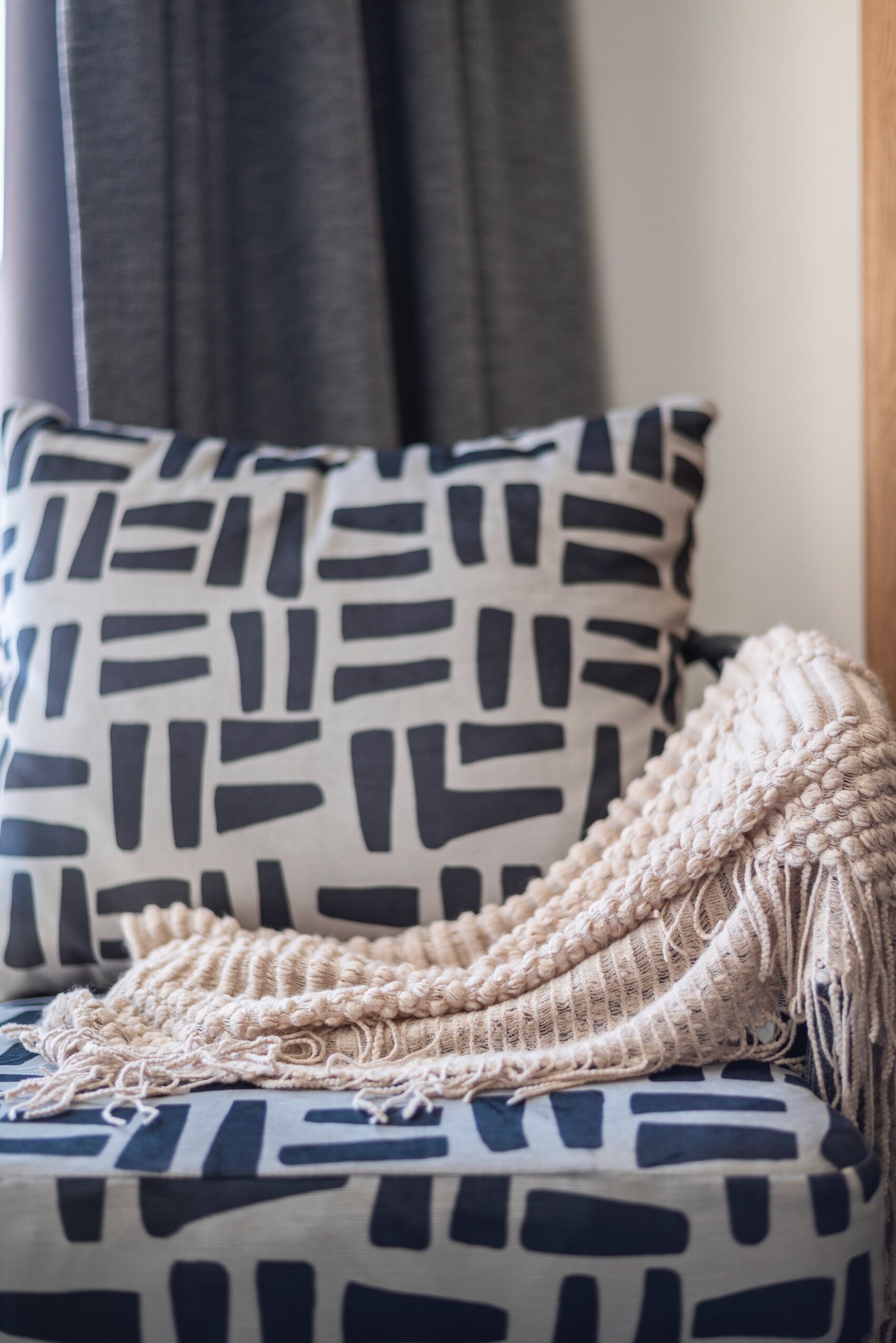 Een kamer met een kussen met een patroon en een macramé plaid op een bank.