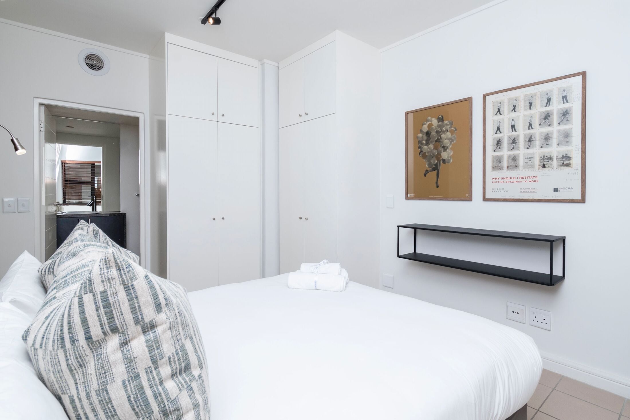 Una camera d'albergo con un letto, un armadio, uno specchio e opere d'arte alle pareti.