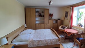 Un dormitorio con cama, una mesita, una silla, un armario y una ventana con cortinas.
