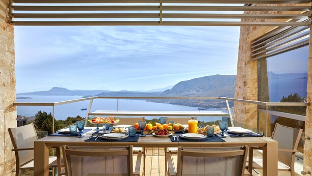 A dining table set with plates, glasses, and fruits, overlooking a scenic view of a lake and mountains. - Olives and Thyme Retreat (Chania)