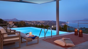 A modern outdoor pool area with a view of the sea and mountains, furnished with a table, chairs, and candles. - Olives and Thyme Retreat (Chania)