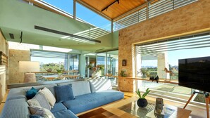 A modern living room with a large sectional sofa, a glass coffee table, and a TV on a tripod stand. - Olives and Thyme Retreat (Chania)