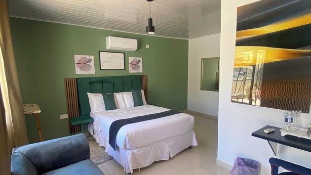 A bedroom with a bed, a sofa, a desk, and a wall with artwork. - Dikukama Hotel (Tshabong)