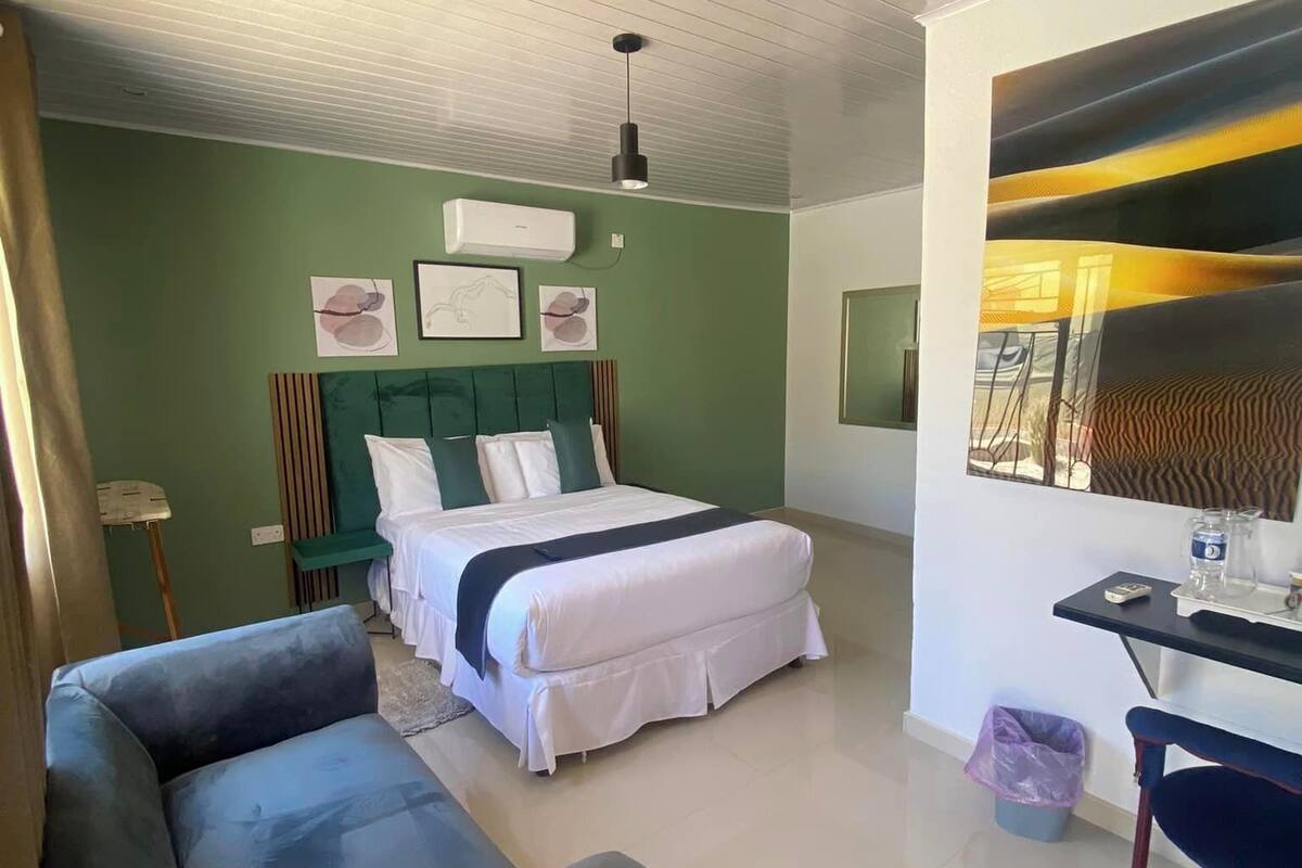 A bedroom with a bed, a sofa, a desk, and a wall with artwork.