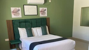 A bedroom with a bed, a green headboard, a bedside table, and a wall-mounted air conditioner. - Dikukama Hotel (Tshabong)