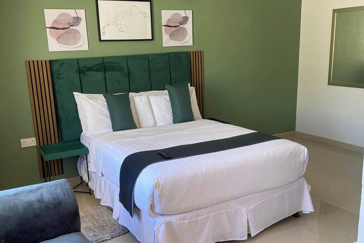 A bedroom with a bed, a green headboard, a bedside table, and a wall-mounted air conditioner.
