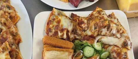 Tres platos de comida que incluyen pizza, carne y rollitos primavera.