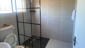 A modern bathroom with a glass-enclosed shower, a toilet, and a sink. - Dikukama Hotel (Tshabong)