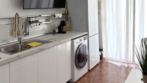 Une cuisine moderne dotée d’un évier en acier inoxydable, d’un lave-linge encastré et d’un téléviseur à écran plat fixé au-dessus du plan de travail.