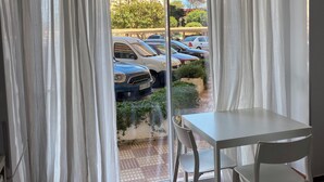 Une pièce dotée d’une porte-fenêtre coulissante donnant sur un espace de stationnement, d’une table blanche et de deux chaises blanches.