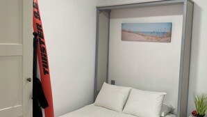 Une chambre avec un lit, un ventilateur de plafond, un tableau représentant une plage et une planche de surf appuyée contre le mur.