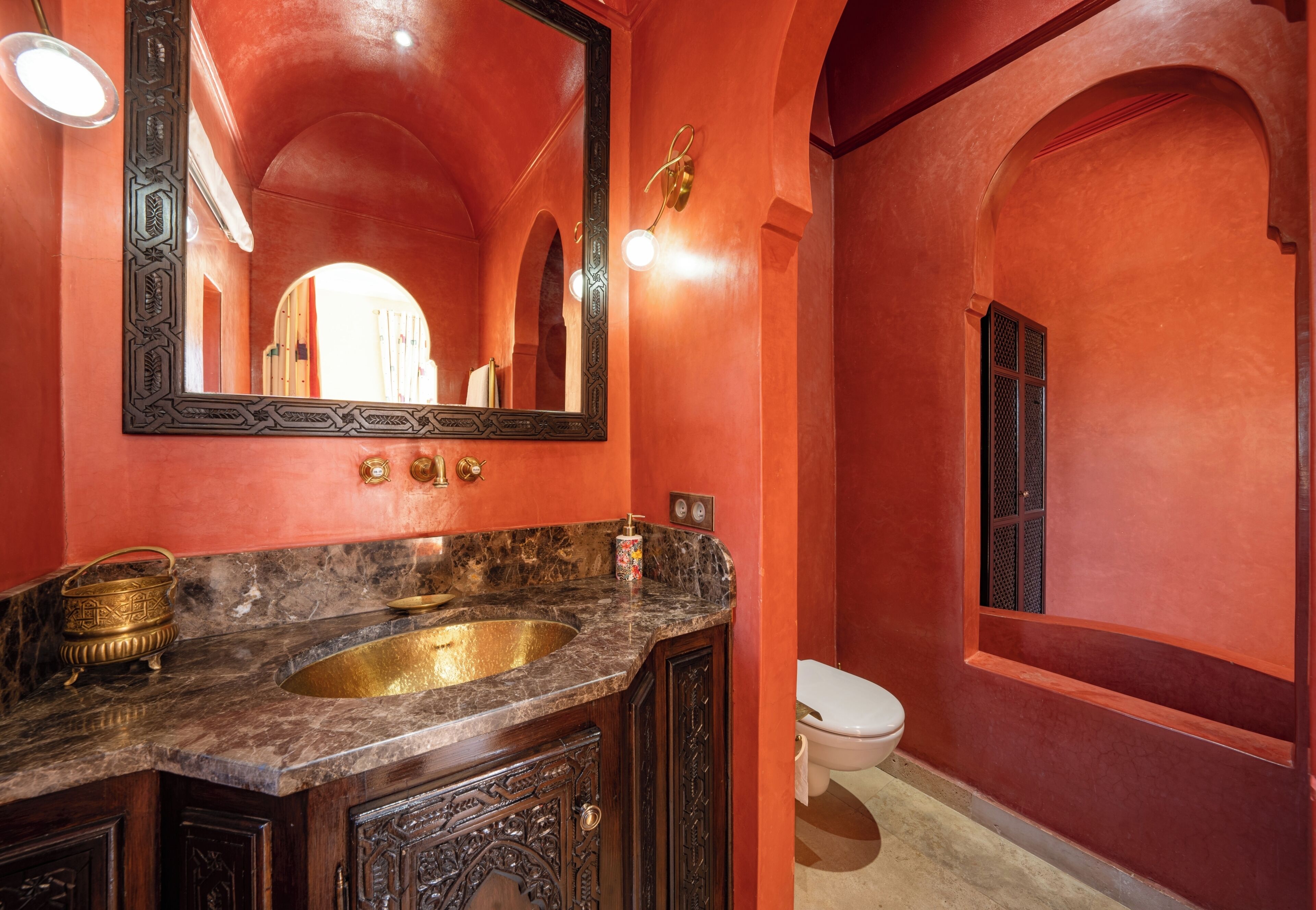 A bathroom with a marble sink, a large mirror, and a red wall.
